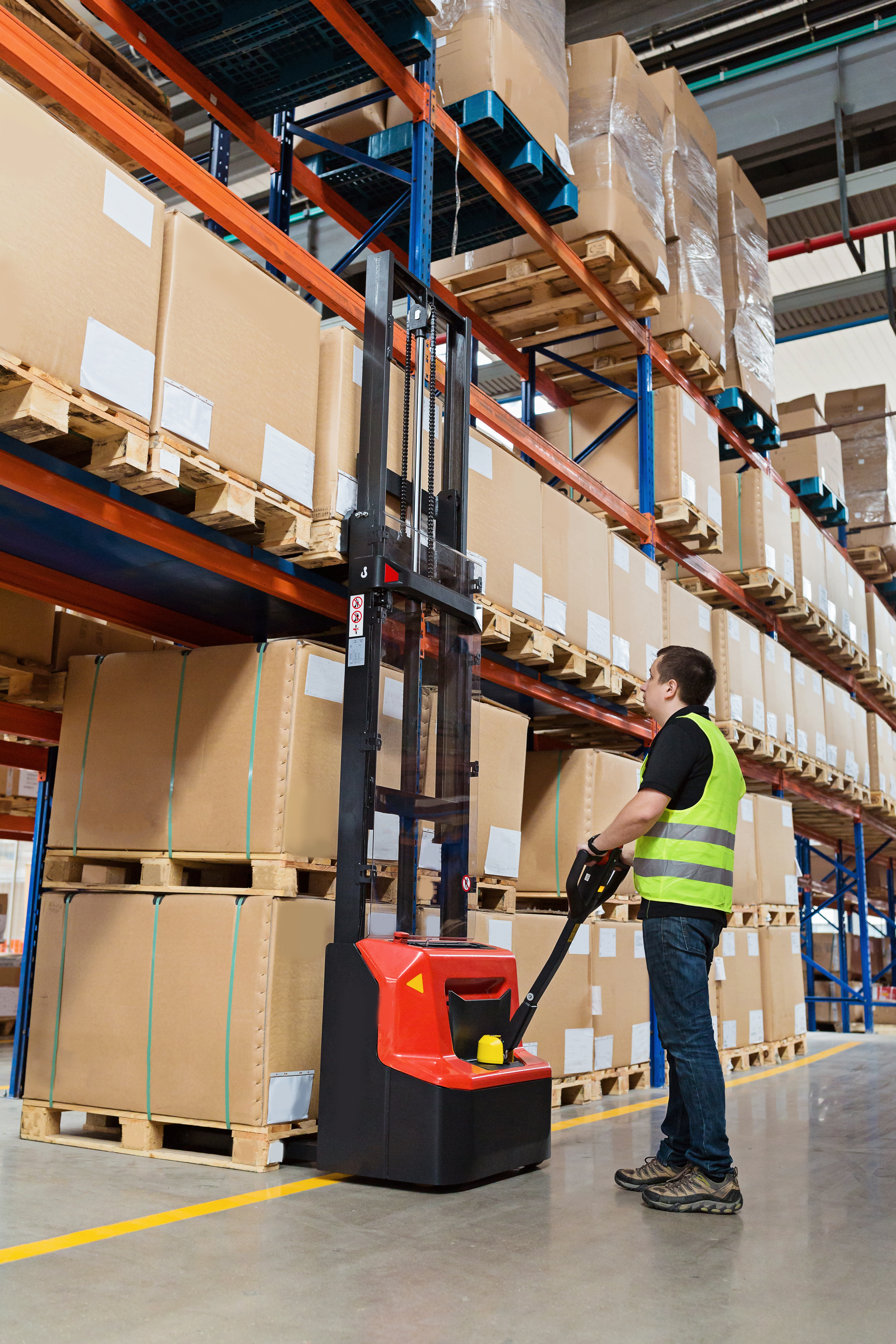 Storehouse man employee in uniform using forklift with box in modern automatic warehouse.Boxes are on the shelves of the warehouse. Warehousing, machinery concept. Logistics in stock.